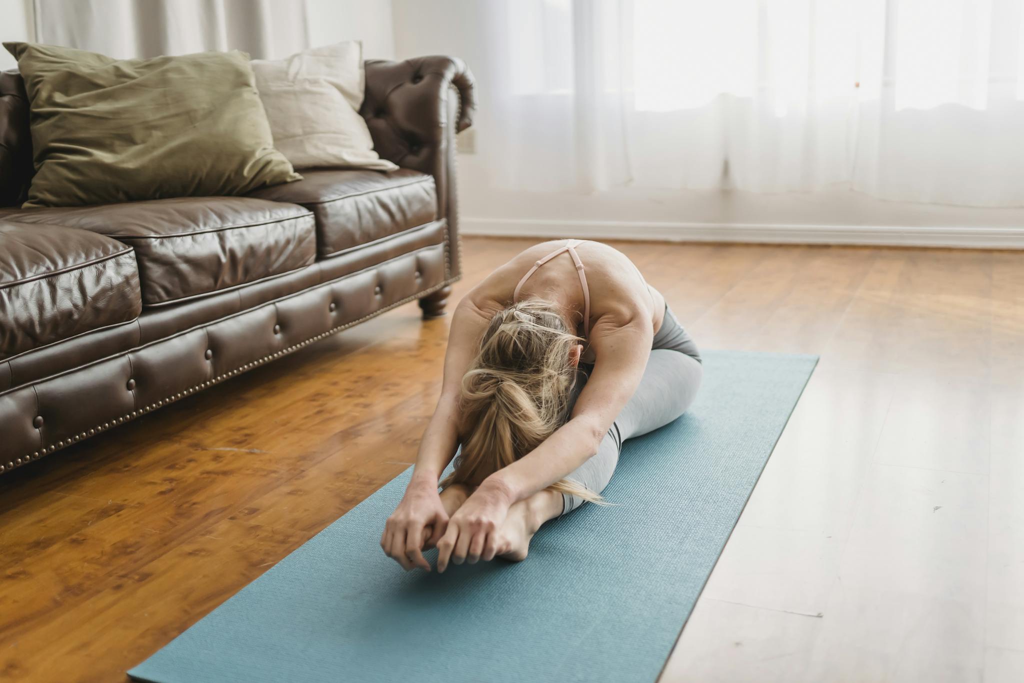 Anonymous female yogi doing Pascimottanasana stretching exercise on mat at home