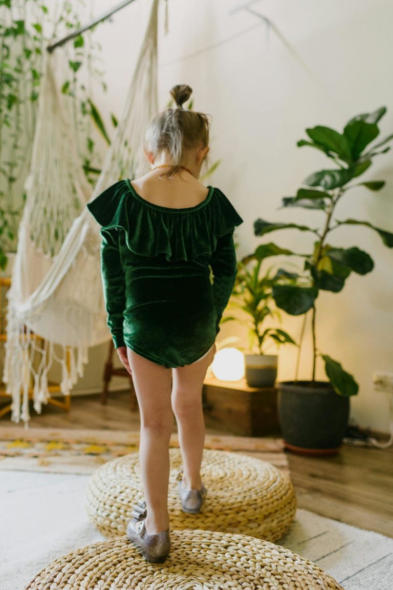 Anonymous little kid standing on straw weaker poufs in stylish home