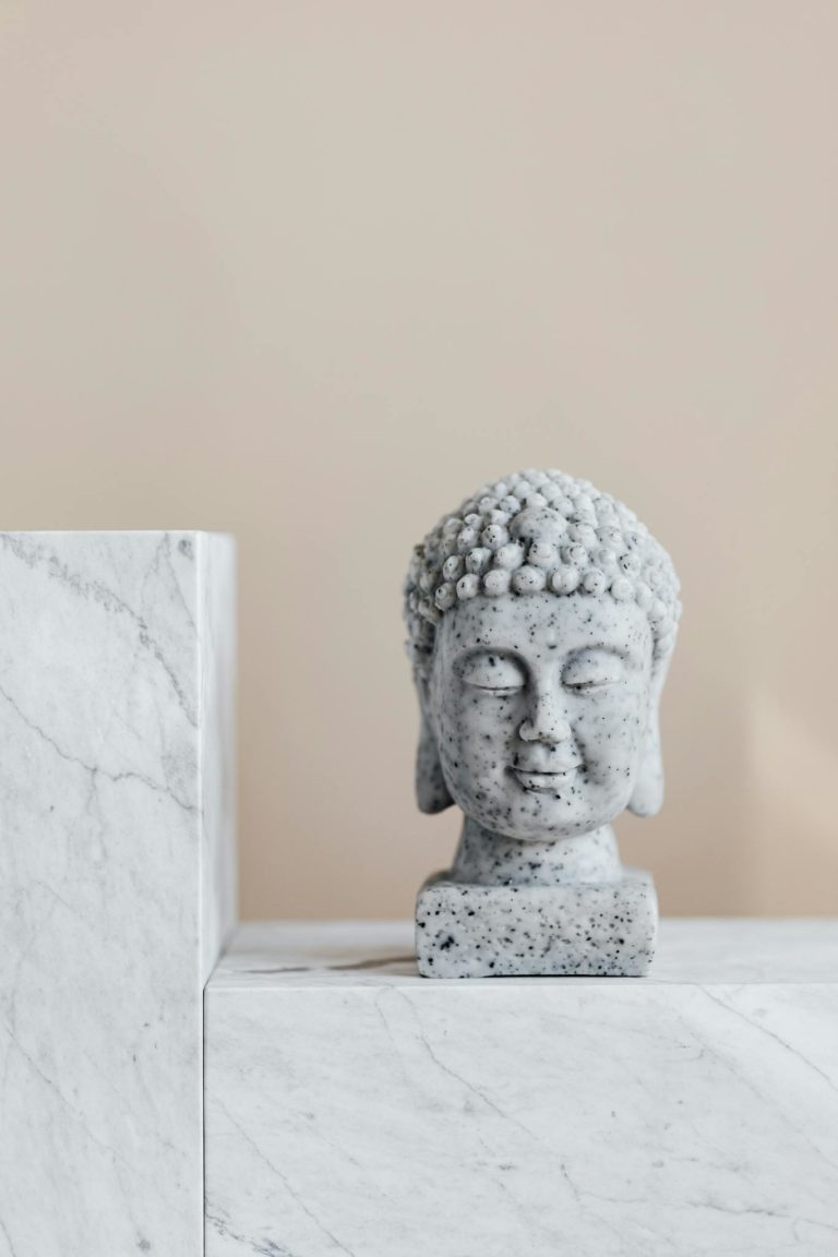 Granite statue of Buddha placed on white marble shelf against beige wall as religion symbol and home decoration element